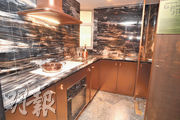廚房屬傳統梗廚設計，牆身和廚櫃面均採用深色石材，並以金銅色櫃門作配襯。（劉焌陶攝）