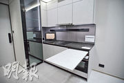 開放式廚房選用灰白色櫥櫃面板、配黑色金屬邊框，附有摺疊餐枱。