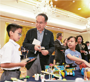 財經事務及庫務局長許正宇（前排中）昨天出席《明報環境、社會及企業管治大獎2025》頒獎禮擔任主禮嘉賓，他並參觀「校園永續未來嘉許禮」的展覽，跟浸信會呂明才小學兩名同學交流校內實踐ESG的成果。昨天共有16間中學和18間小學代表出席嘉許禮。