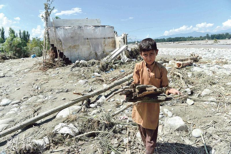 巴基斯坦一名兒童在河畔爛屋旁撿起木塊。當地夏季曾出現河水氾濫。（法新社）