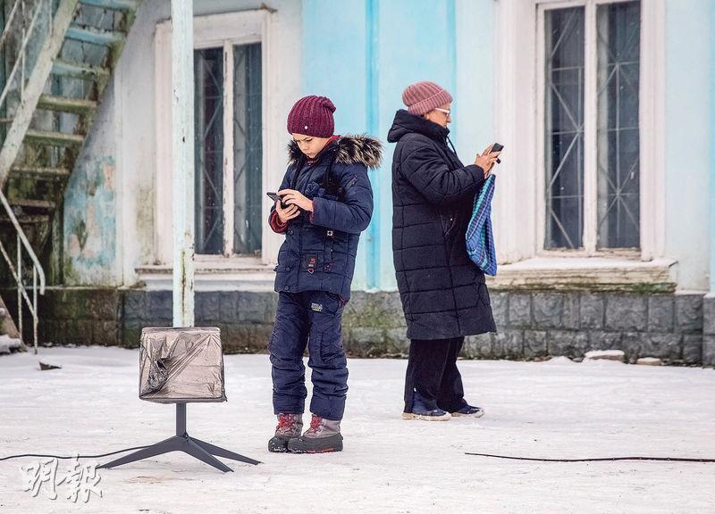 今年1月，在烏克蘭東部頓湼茨克州的查西夫雅爾城鎮，兩名當地居民站在Starlink 終端機旁使用手機。（路透社）