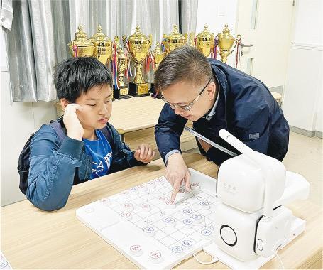 和AI對弈——上海第六師範學校附屬小學新添置了AI象棋機械人，學生向青小校長程志祥（右）示範如何操作。（受訪者提供）