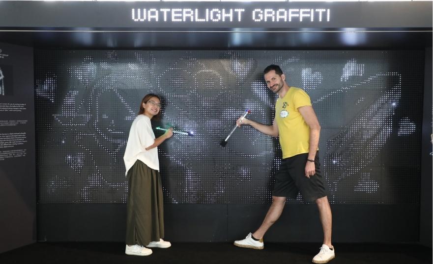 香港藝術家何文蕙（Bao Ho，左）於法國藝術家安東納．傅黑諾（Antonin Fourneau）創作的互動藝術裝置《水燈塗鴉》作畫，通過藝術體現跨港法文化的交流。（圖片由相關機構提供）