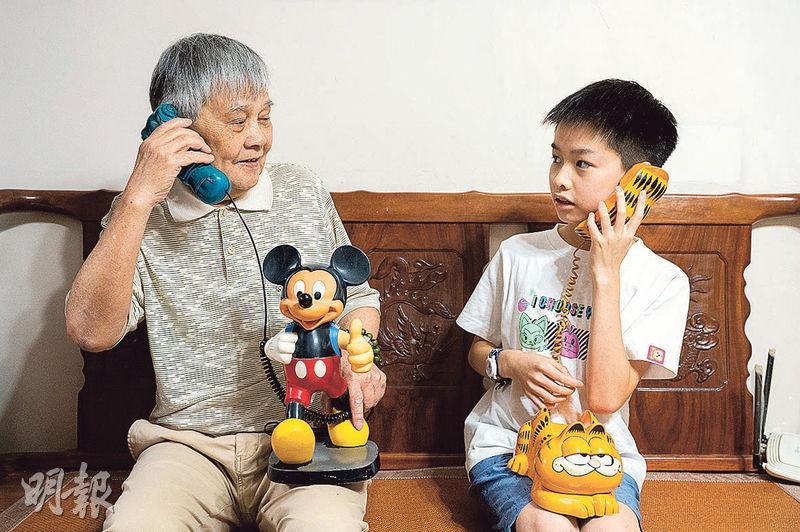 李鈞祥（左）與孫兒Marcus手上的電話均是1980年代於香港製造、外銷至歐美的產品，需換零件後方可在港使用。（朱安妮攝）