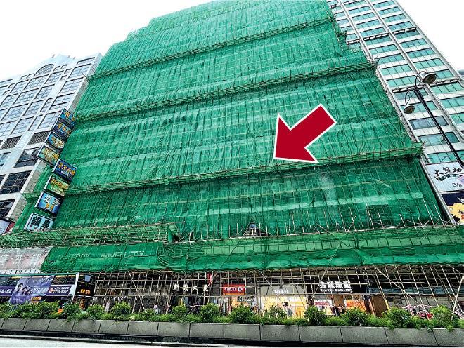 現正進行外牆打鑿工程的旺角新興大廈外牆棚架被綠網包圍，大約每5層樓再外搭一個斜柵（箭嘴示），以防工程中有物件墜落，「每隔3層樓（設斜柵）會再安全啲，𠵱家有啲疏，個圍網望上去無特別加厚」，香港測量師學會建築政策小組主席何鉅業說。