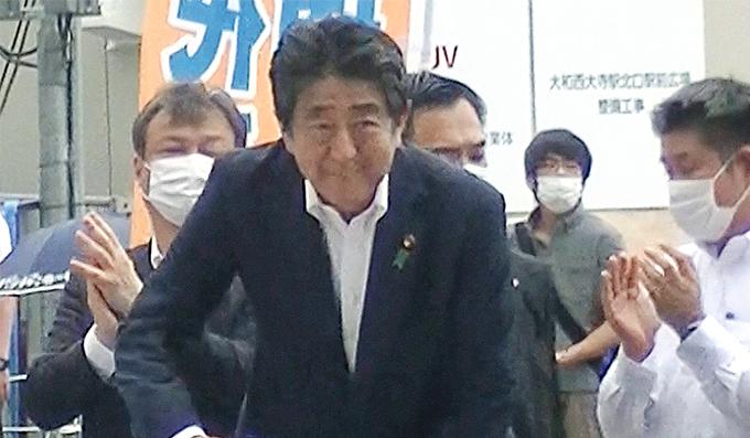 日本《每日新聞》拍到安倍晉三在奈良市遇襲前，穿灰衣的疑犯（後右二）斜揹着武器站在附近伺機攻擊。（明報資料室）