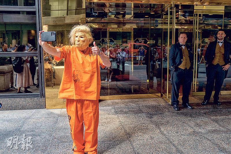 美國前總統特朗普官司纏身。上周三在紐約市的特朗普大廈正門前，有人假扮穿著橙色囚衣的特朗普豎起拇指。（法新社）