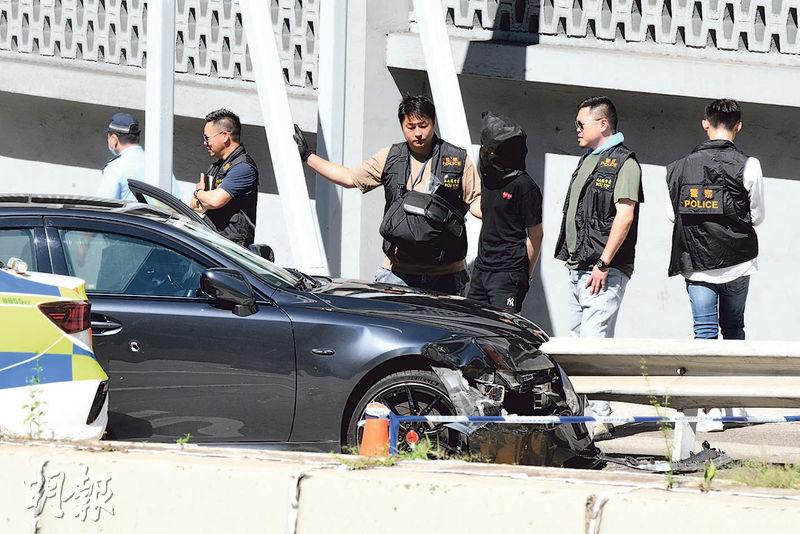 被捕男子被黑布蒙頭，由警員押返涉事私家車附近蒐證。現場所見，私家車頭損毁，右邊車門有一個彈孔。（衛永康攝）