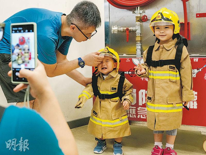 有家長替子女穿上「消防制服」拍照留念，幼童突然嚎啕大哭，家長上前安慰。（楊柏賢攝）