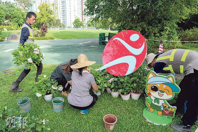 康文署人員噚日趕工整理公園設施，喺園內外增設康文署標誌，代表收回嘅部分粉嶺高球場成為公眾享用嘅政府公園，工人並擺放盆栽，同埋康文署吉祥物「活力仔」（圖右下方）和「思文喵」卡通牌。（朱安妮攝）