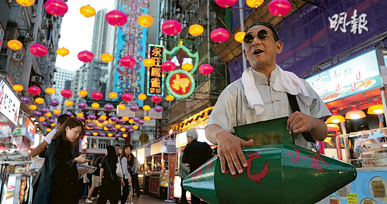 夜市包括7檔懷舊小食流動攤檔，當中有檔販持綠色欖形鐵箱，叫賣香港昔日小食「飛機欖」。（楊柏賢攝）