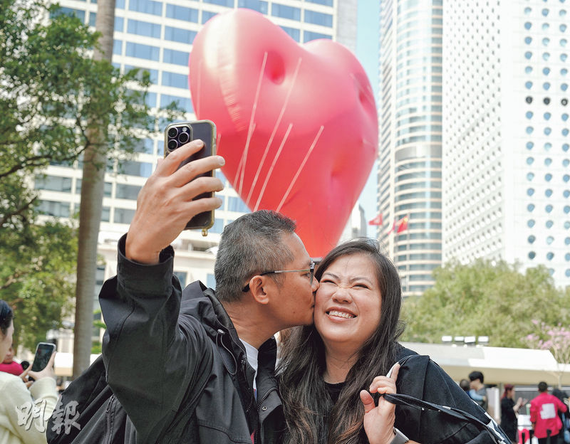 市民陳氏夫婦昨日特意到中環與Chubby Hearts拍照「放閃」，二人認為飄浮紅心很特別和「應節」，笑稱「唔使錢有得睇，經濟實惠」。（鍾林枝攝）