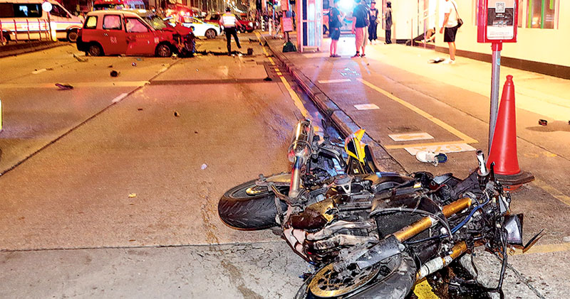 疑因衝燈遭猛撼的電單車嚴重損毁，滑行約20米後在行人路旁翻側，涉事的士橫亙路中，警方事後封鎖行車線與行人路調查。